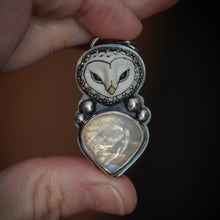 Load image into Gallery viewer, Silver pendant with owl design and heart-shaped stone held between fingers against a dark background

